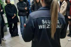 Zdjęcie grupowe w części administracyjnej aresztu, spotkanie z funkcjonariuszką w umundurowaniu uczestników spotkania.
