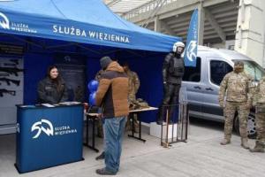 Stoisko promocyjne Służby Więziennej wraz z funkcjonariuszami i odwiedzającymi.
