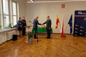 W sali obok flag, stoją funkcjonariusze
